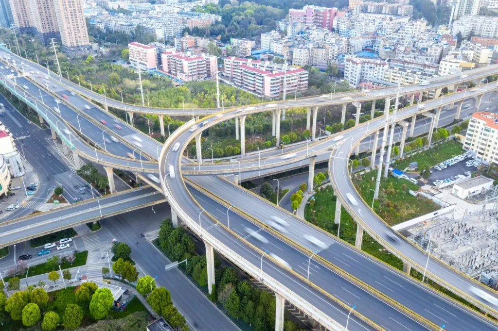 Malaysia Infrastructure Investment Strategies: Aerial view of a complex highway interchange surrounded by buildings and greenery, showcasing multiple winding roads and traffic movement.