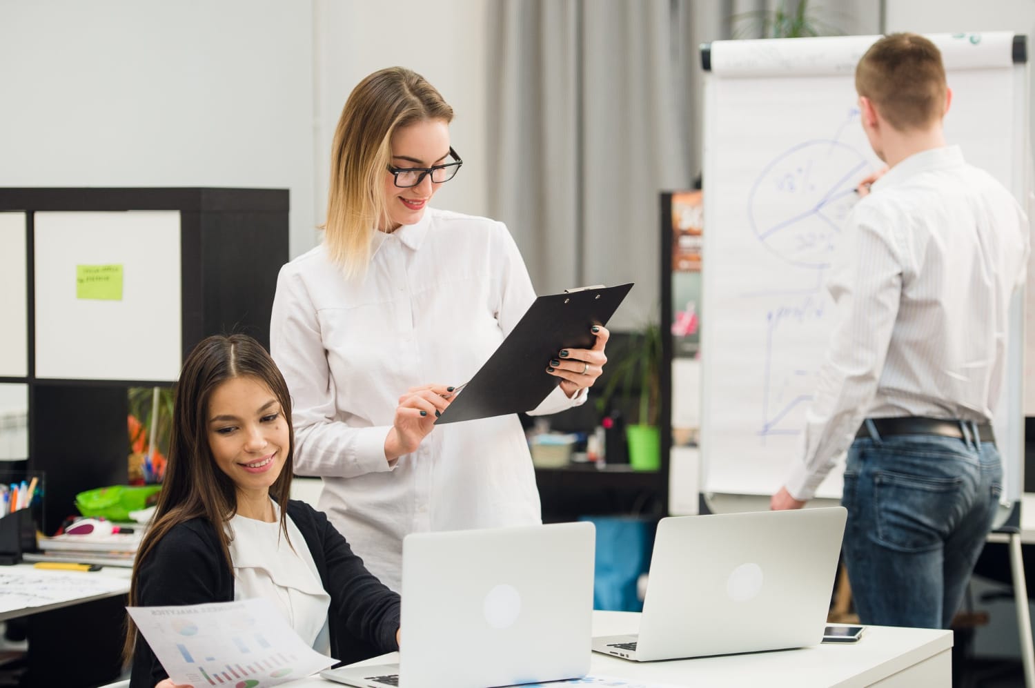 Market Entry Strategies: Office workers with laptops discussing near a whiteboard.