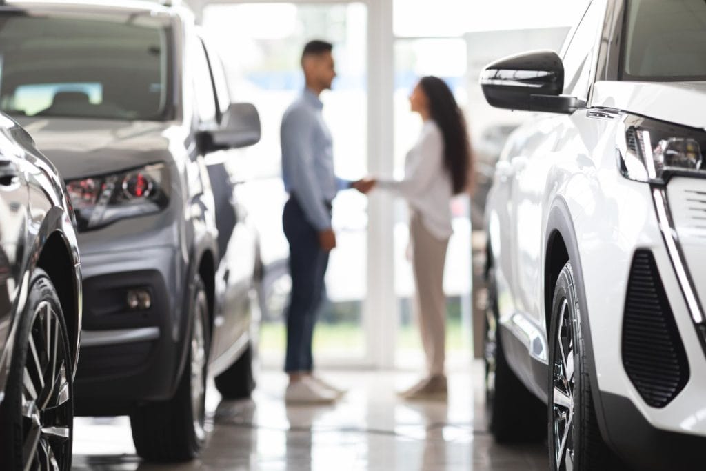 A car dealership interior featuring two individuals shaking hands, with various cars displayed in the foreground and background to show Middle East Auto Market Trends