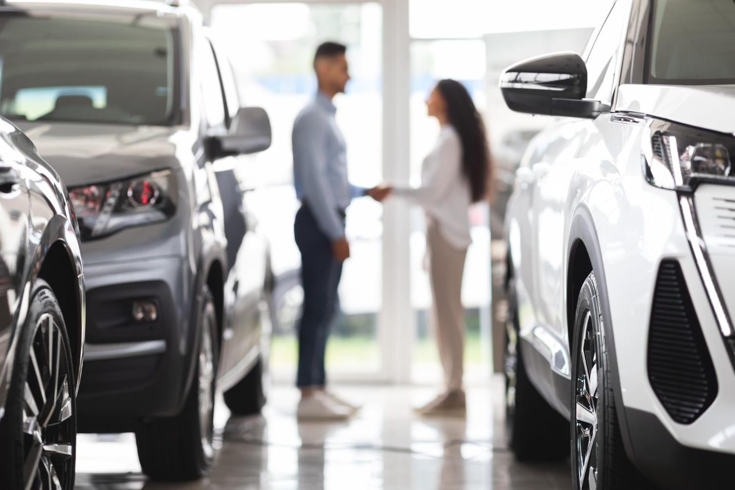 A car dealership interior featuring two individuals shaking hands, with various cars displayed in the foreground and background to show Middle East Auto Market Trends