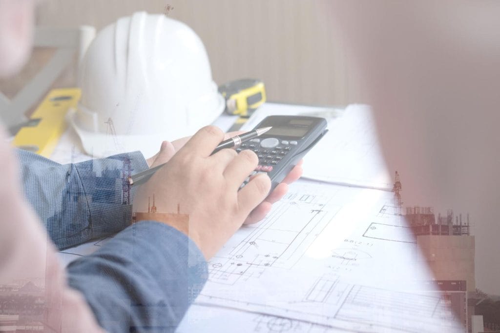 Indonesia Construction Financing Strategies: A person using a calculator and pen while reviewing construction plans, with a hard hat and measuring tools in the background.