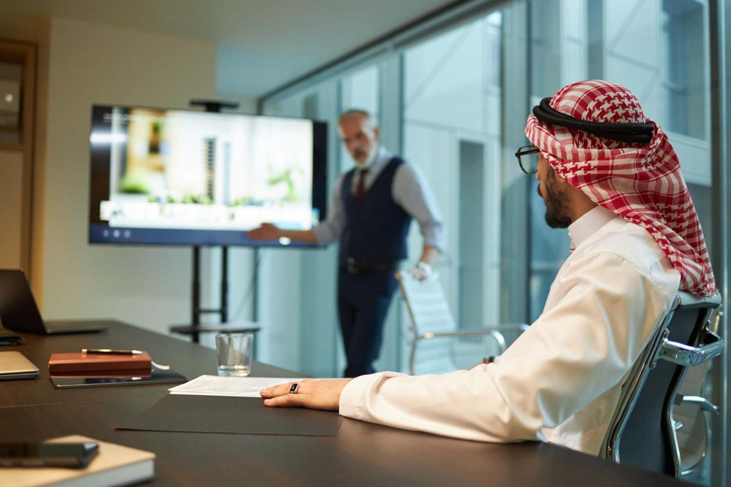 Eurogroup Consulting Middle East: A businessman in traditional attire sits at a conference table attentively watching a presentation on a large screen.