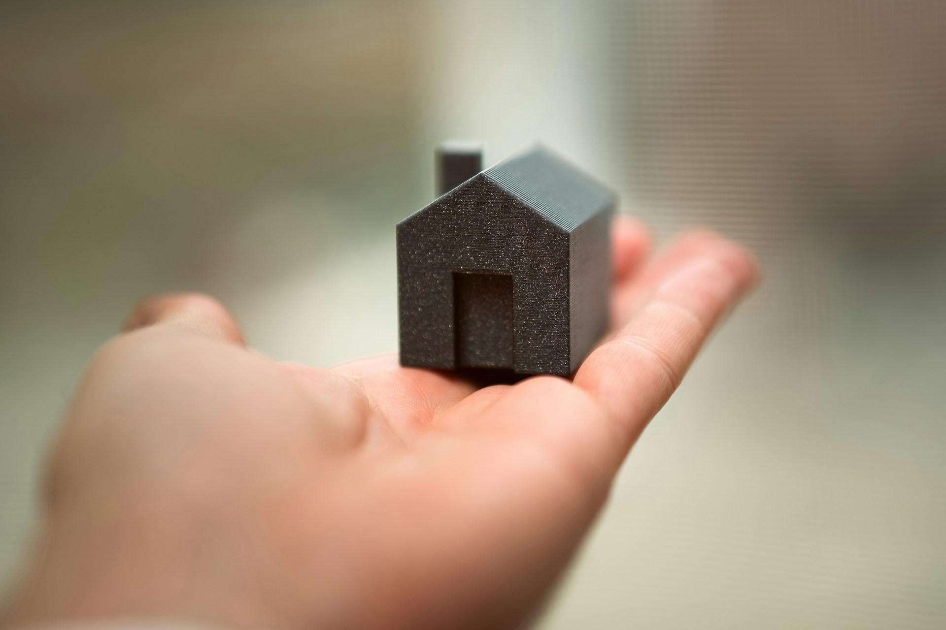 Real Estate Investment Trends: A hand holds a small, dark, textured model of a house, showcasing the intricate details of its design against a soft background.