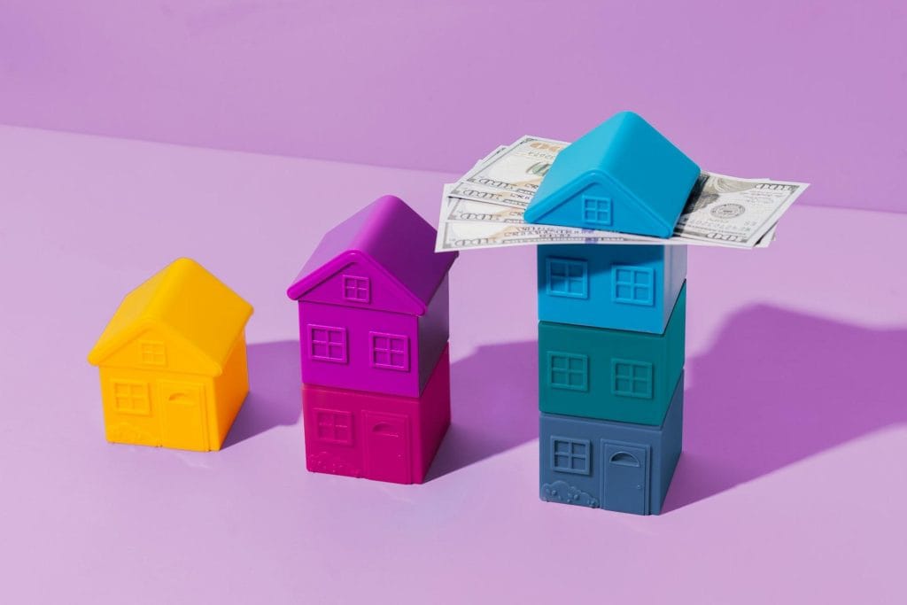 Malaysia Real Estate Investment Trends: Colorful toy houses stacked with cash on top, set against a purple background, symbolizing real estate and financial growth.
