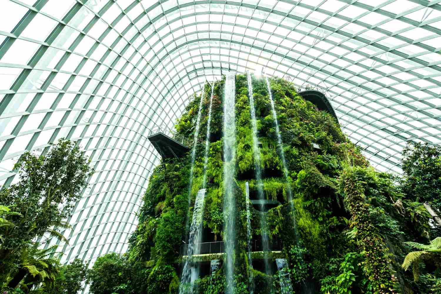 Singapore Green Building Certifications: A stunning indoor waterfall cascades over a lush, green mountain surrounded by glass architecture, creating a vibrant tropical oasis.