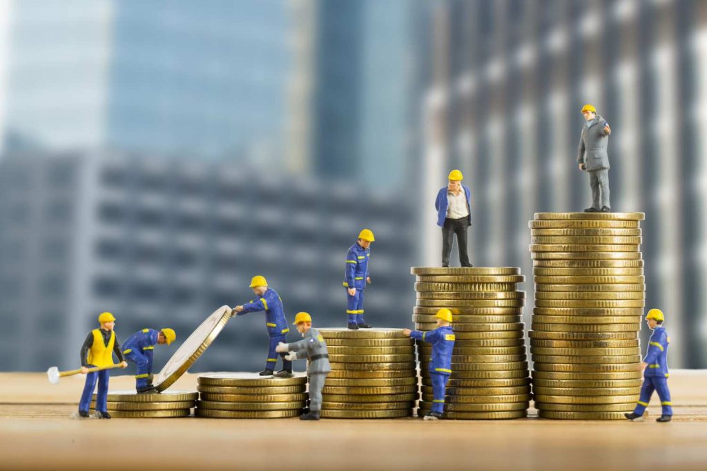 Malaysia Construction Financing Challenges: Miniature construction workers are stacking coins, representing financial growth and teamwork against a blurred city backdrop.