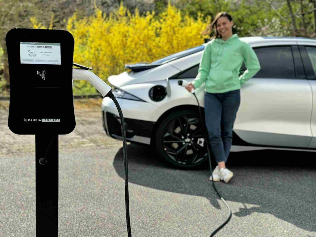 Indonesia Battery Downstream Project: A person stands next to a sleek electric vehicle, connecting a charging cable to the car at an electric vehicle charging station.