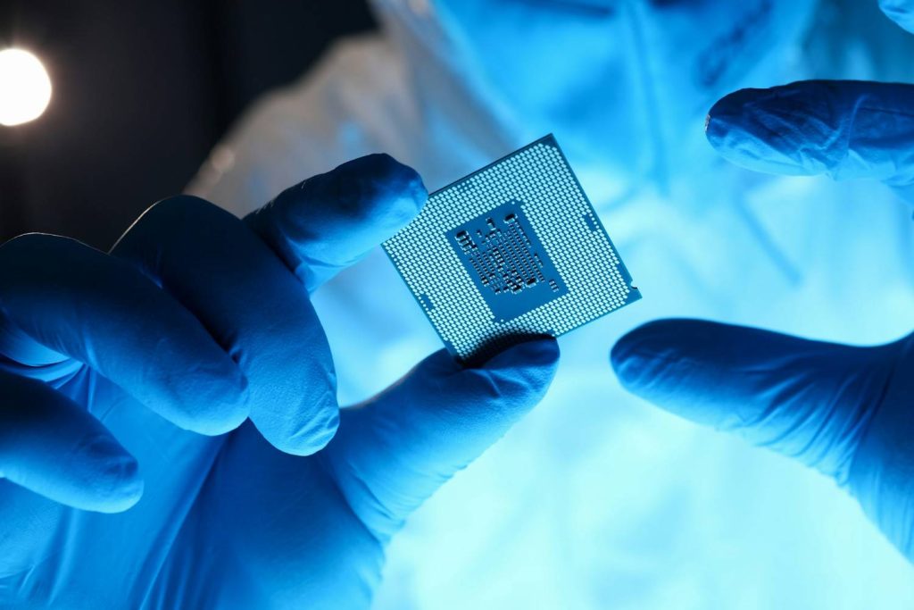 India Chip Manufacturing: A gloved hand holds a shiny computer processor under blue lighting, emphasizing precision and technology in a lab environment.