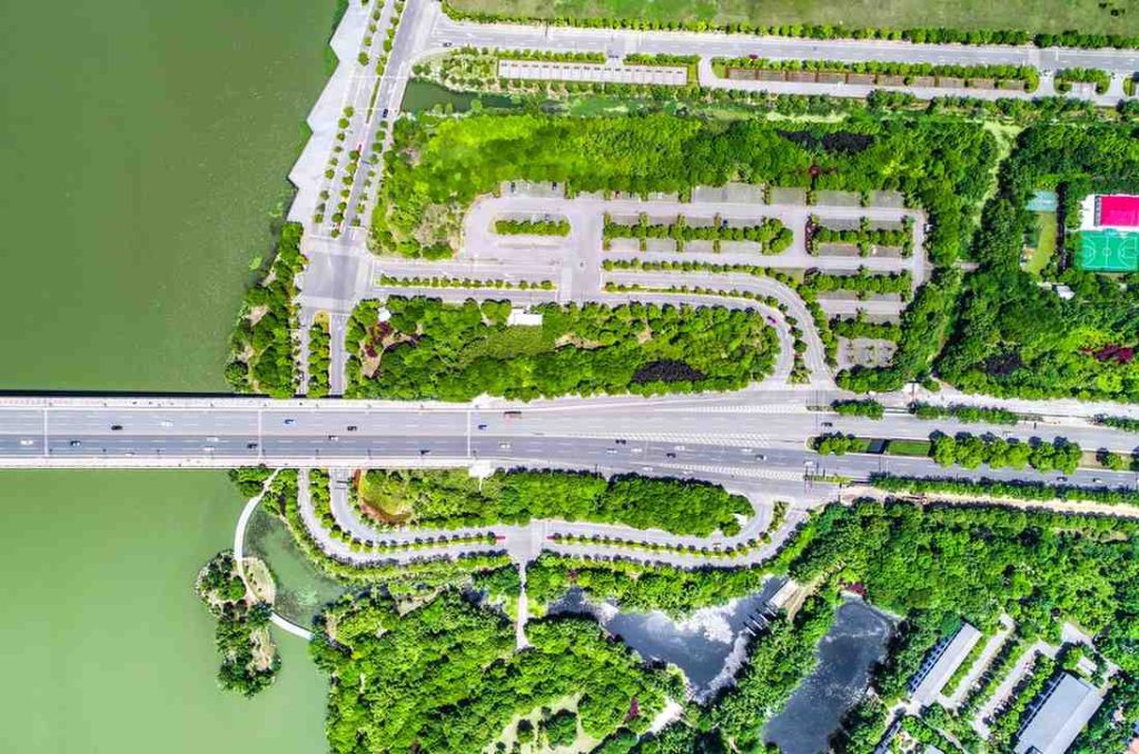 Philippines Green Infrastructure Projects: Aerial view of a green park area bordered by a road and a lake, featuring winding paths, trees, and a sports court in the background.