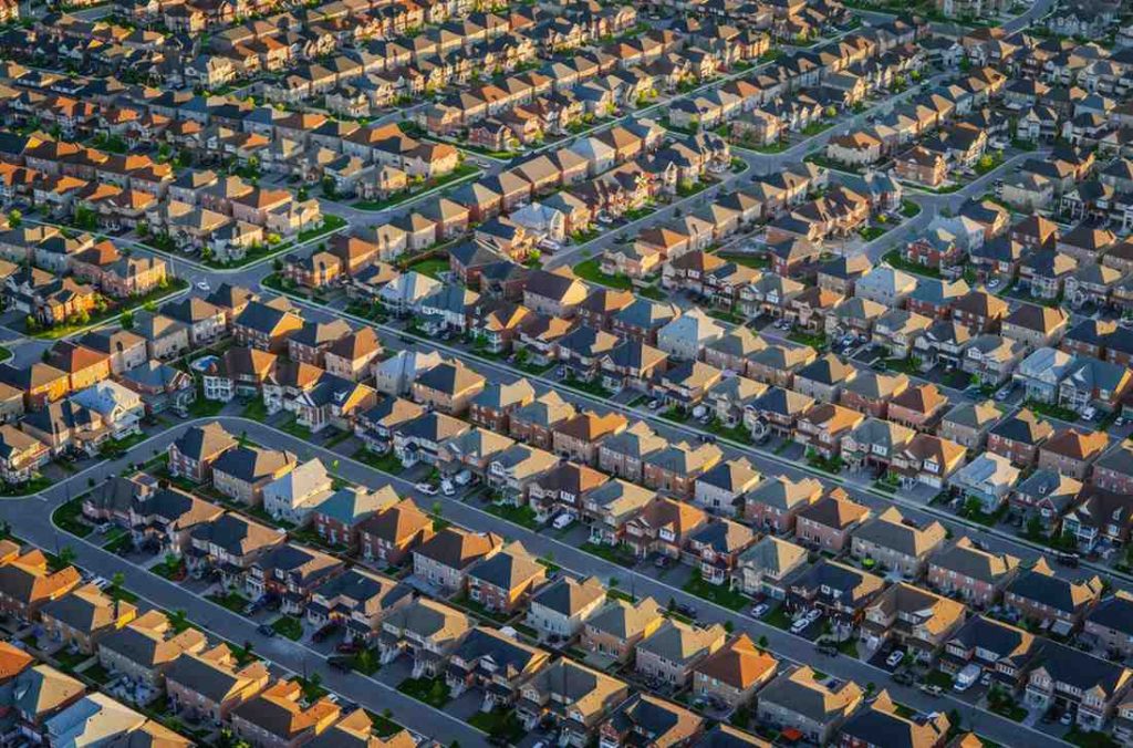 Singapore Urbanization and Housing Demand: Aerial view of a suburban neighborhood featuring rows of houses with varied roof colors and lush green lawns.