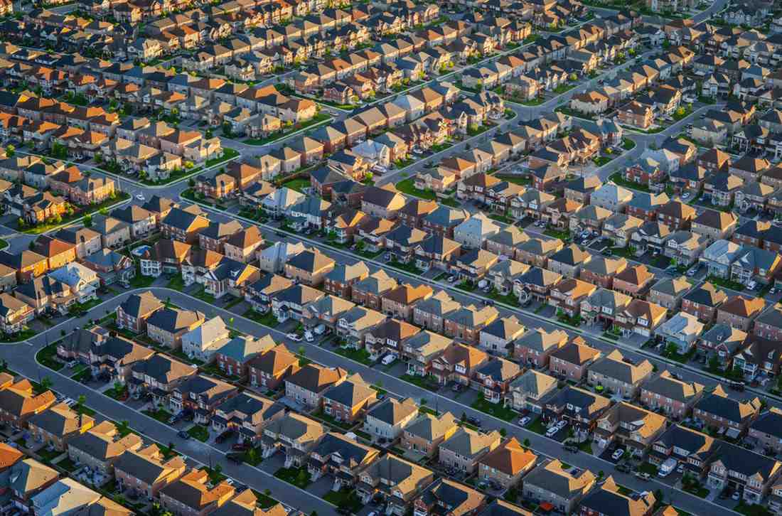 Singapore Urbanization and Housing Demand: Aerial view of a suburban neighborhood featuring rows of houses with varied roof colors and lush green lawns.